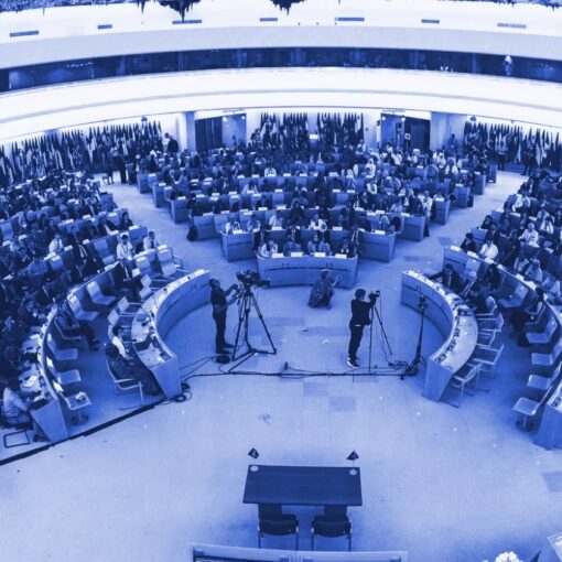 Imagem da sala de conferências da OIT. Lugares dispostos em circulos e onde estão sentados os representantes dos Estados Membros. A sala está com luz ambiente luz.