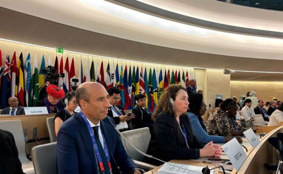 Sala de reuniões da OIT em Geneve com os representantes de Portugal. Bandeiras dos paises representantes no fundo da sala