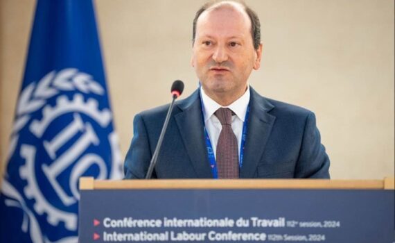 Foto do Secretário de Estado a fazer a sua intervenção no pulpito. Bandeira da OIT no fundo da sala e nas suas costas