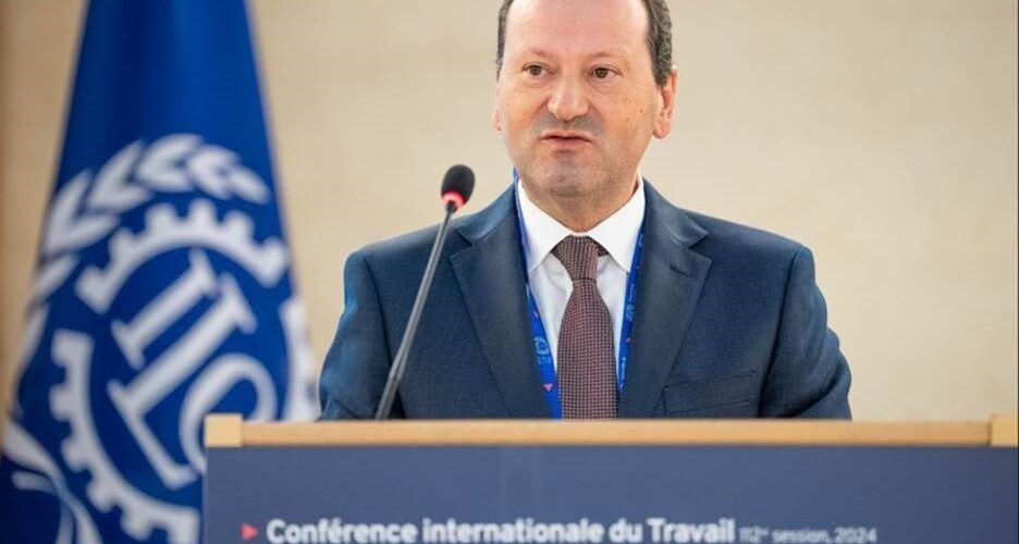 Foto do Secretário de Estado a fazer a sua intervenção no pulpito. Bandeira da OIT no fundo da sala e nas suas costas